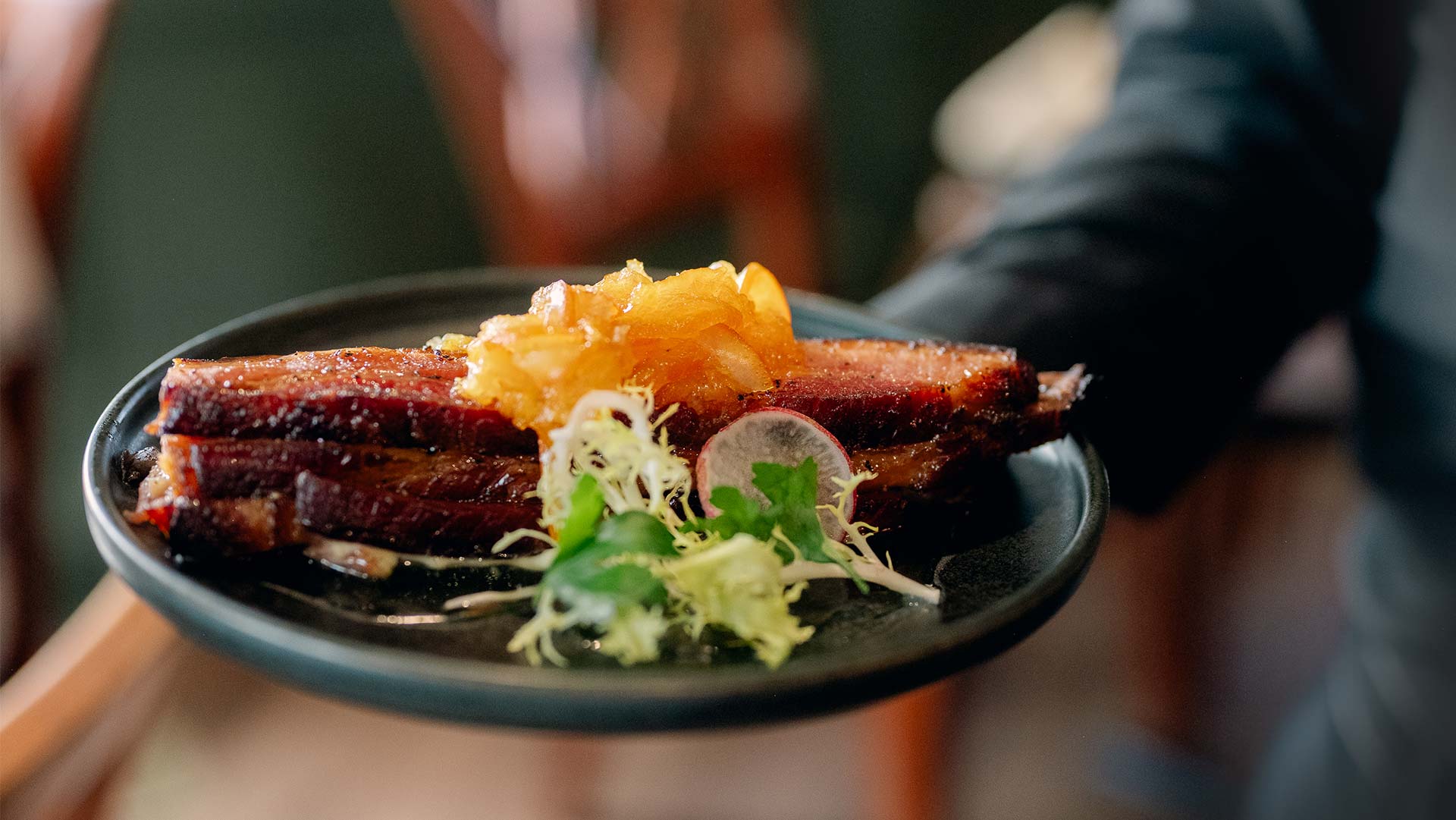 Person serving delicious food on black plate